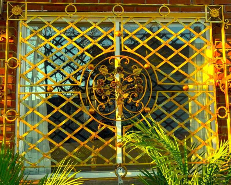 Gilded lattice window guard with a forged rose medallion on a red brick house