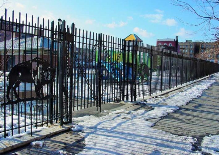 Black park fence and gate carrying a cut animal silhouette beside playground equipment