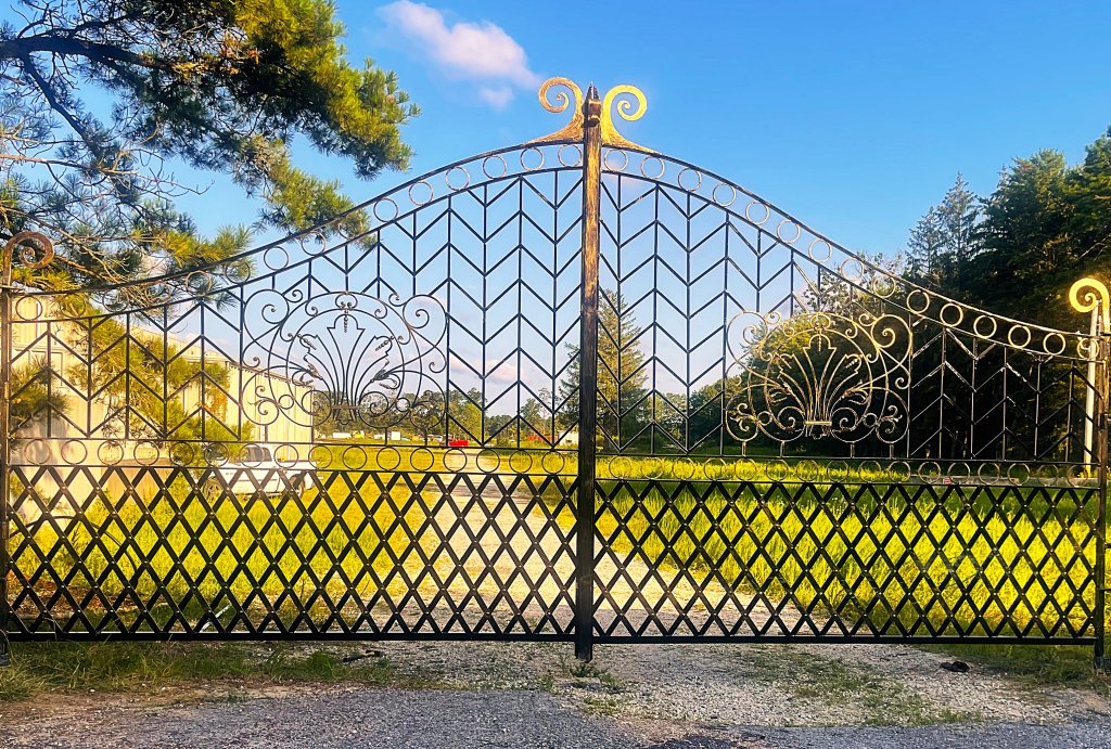 Black and gold garden gate with chevron panels and diamond lattice under blue sky