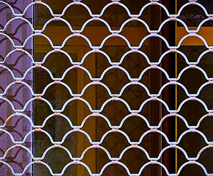 White painted seashell pattern grille over dark storefront glass with amber reflections