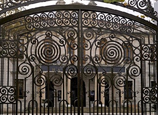 Dark scrolled iron gate of tight spirals in front of a pale stone building