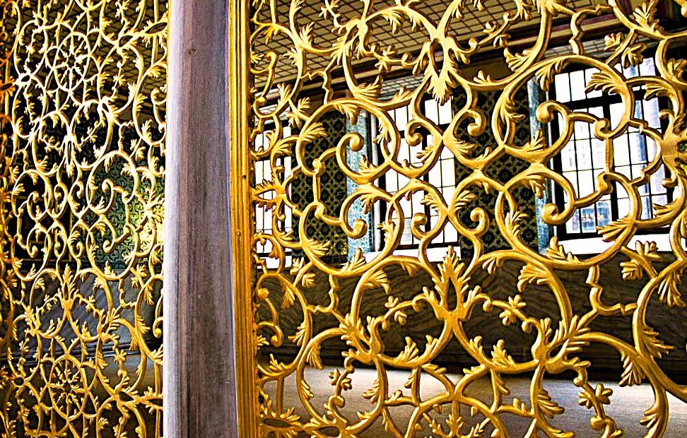Gilded bronze screens of scrolling leaves flanking a stone column, leaded windows beyond
