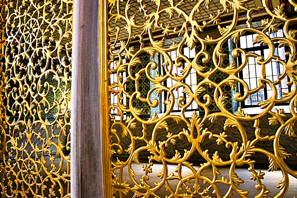 Gilded bronze screens of scrolling leaves flanking a stone column, leaded windows beyond