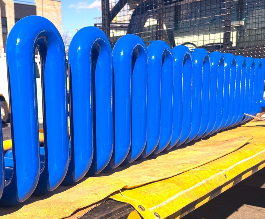 Row of glossy blue pipe bends standing on a truck bed under blue sky