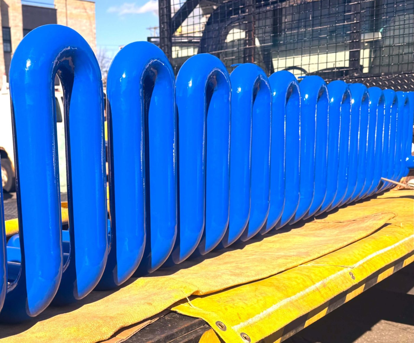 Row of glossy blue pipe bends standing on a truck bed under blue sky