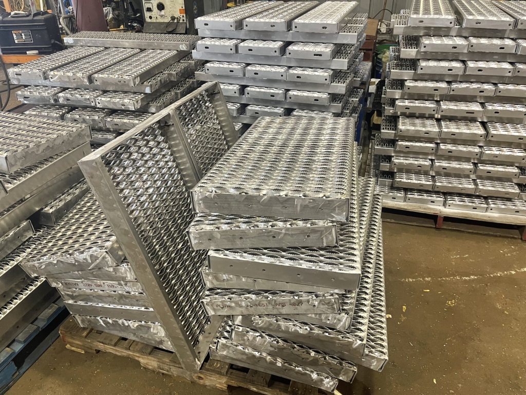 Stacked aluminium stair treads and grip plate panels on pallets inside the workshop