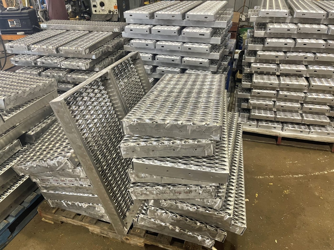 Stacked aluminium stair treads and grip plate panels on pallets inside the workshop