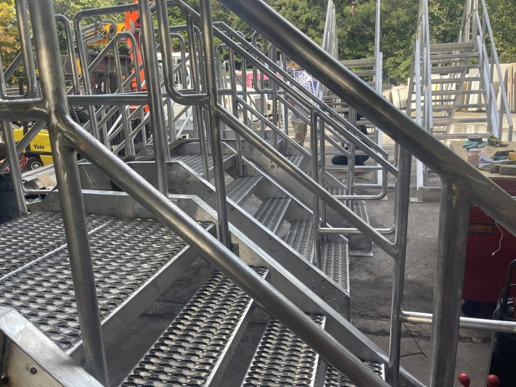 Close view up an aluminium stair flight with perforated treads and welded tube handrails