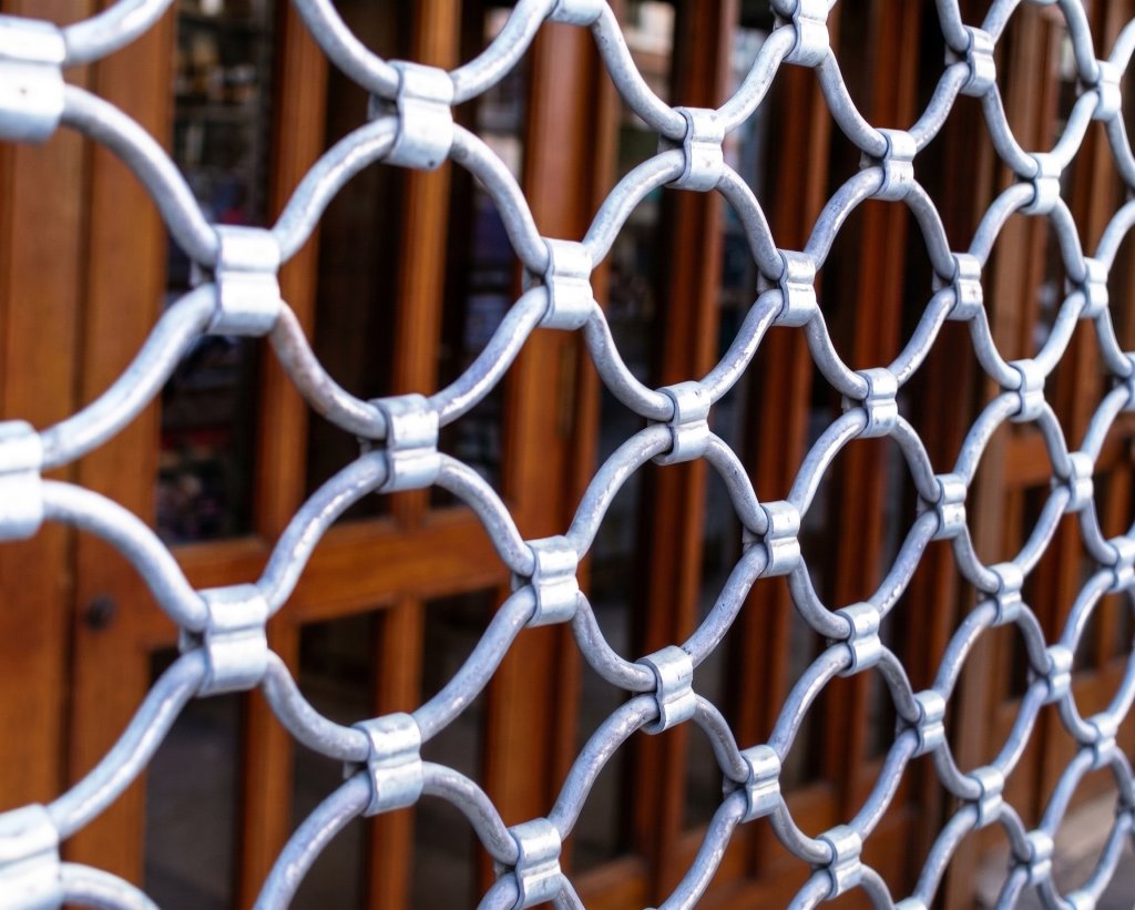 Silver-grey O-ring grille closing a storefront, warm timber door frames behind
